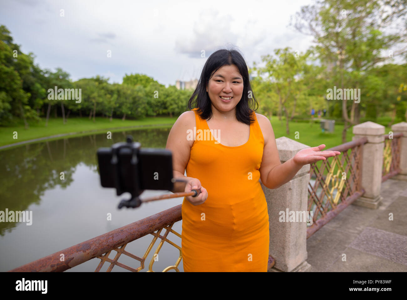 Donna asiatica tenendo selfie con telefono cellulare allega a selfie stick in posizione di parcheggio Foto Stock