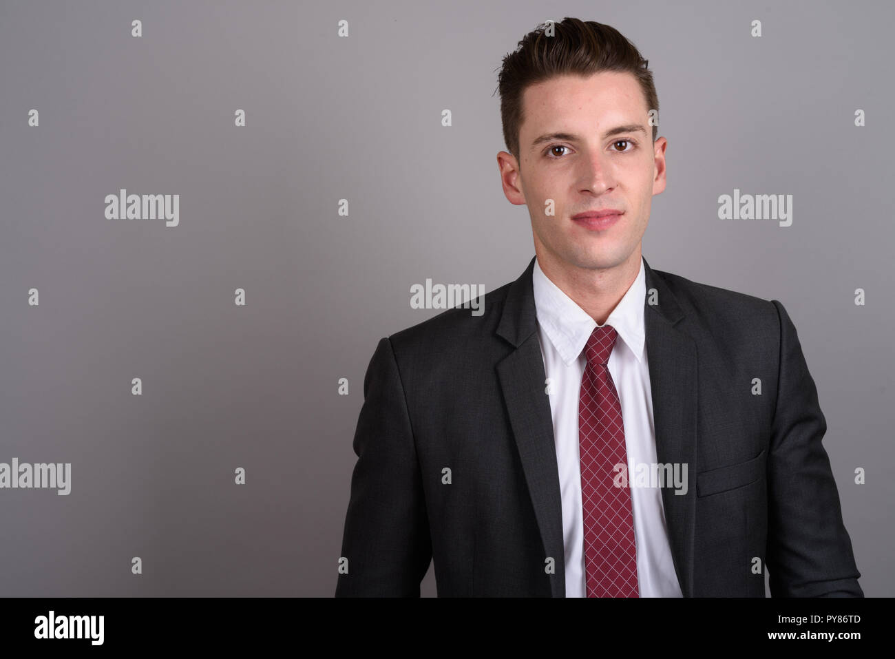 Giovane imprenditore bello indossare tuta contro uno sfondo grigio Foto Stock