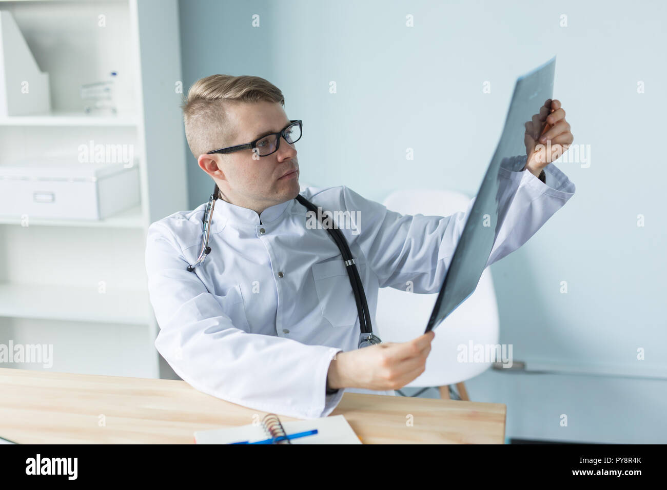 Giovane medico caucasica seduta nel suo ufficio e alla ricerca di immagini a raggi X Foto Stock