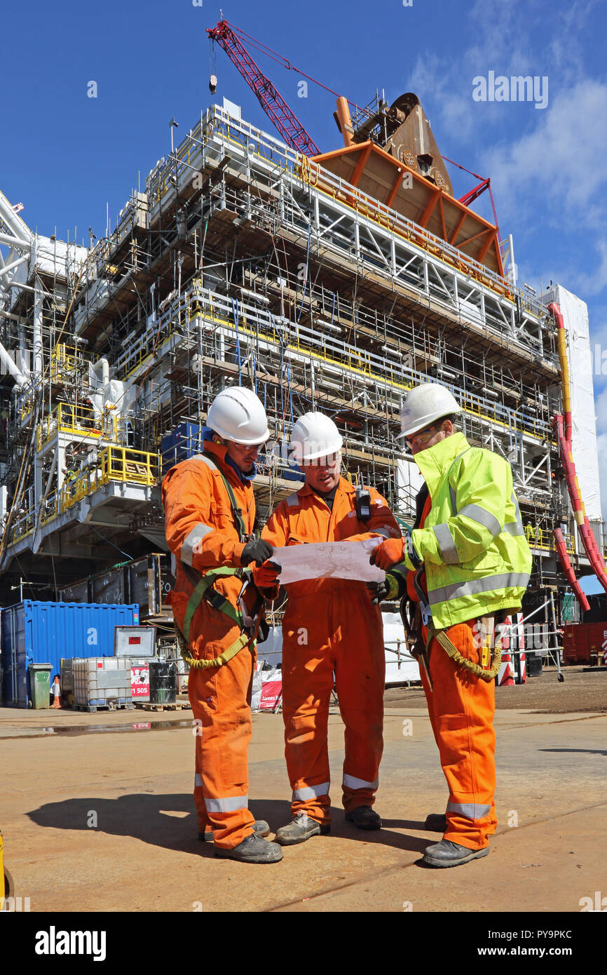 3 ingegneri discus un disegno durante la costruzione di un gas offshore della piattaforma di produzione nel Mare del Nord porto di Hartlepool, Regno Unito Foto Stock