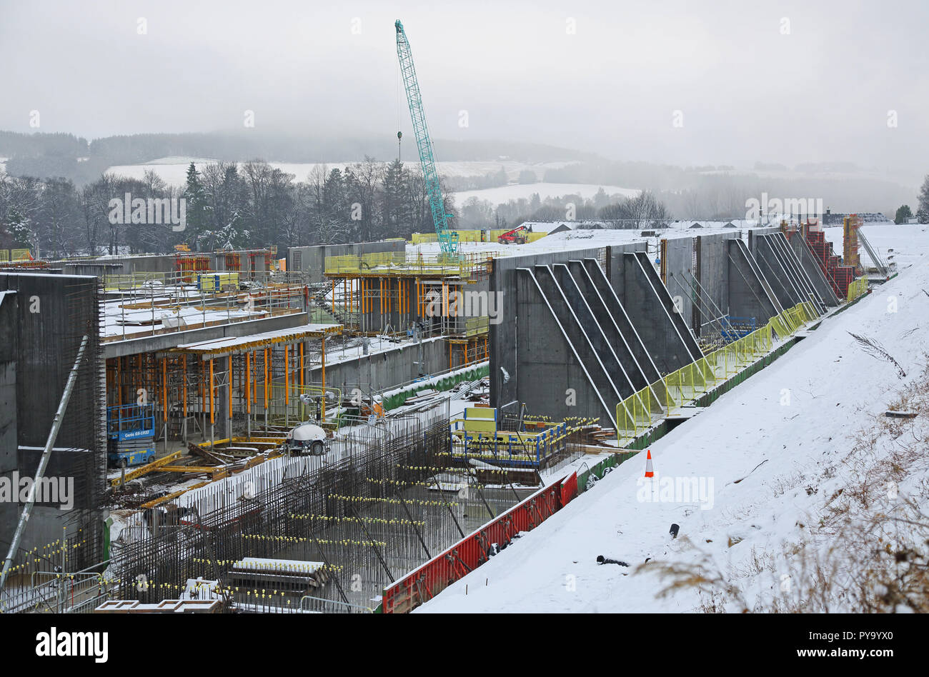 Un grande sito di costruzione in Scozia con il lavoro interrotto dalla forte nevicata. Mostra grandi pannelli per casseratura per la costruzione delle alte pareti di cemento. Foto Stock