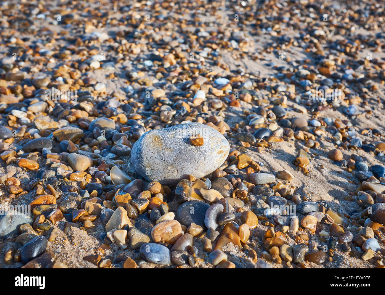 Close up di un gran sasso con un piccolo ciottolo sulla parte superiore circondata da più piccoli ciottoli su una spiaggia con sabbia al di sotto Foto Stock