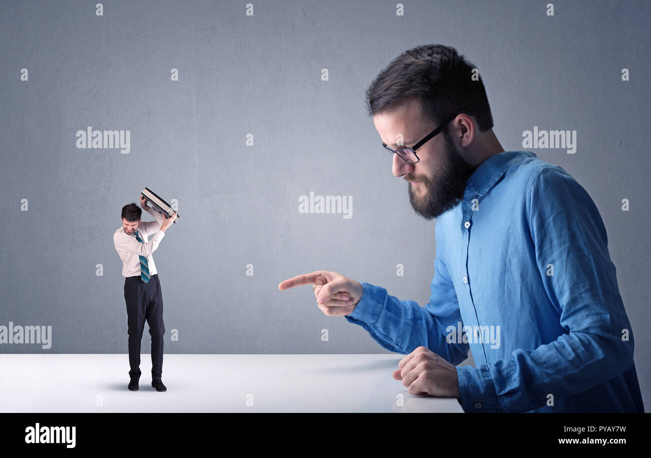 Giovane imprenditore professionale essendo arrabbiato con un altro imprenditore in miniatura nella parte anteriore di un bluastro sfondo grigio Foto Stock
