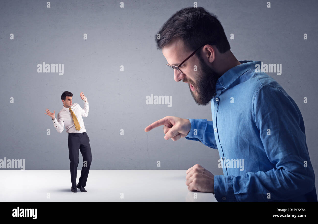 Giovane imprenditore professionale essendo arrabbiato con un altro imprenditore in miniatura di fronte a uno sfondo grigio Foto Stock