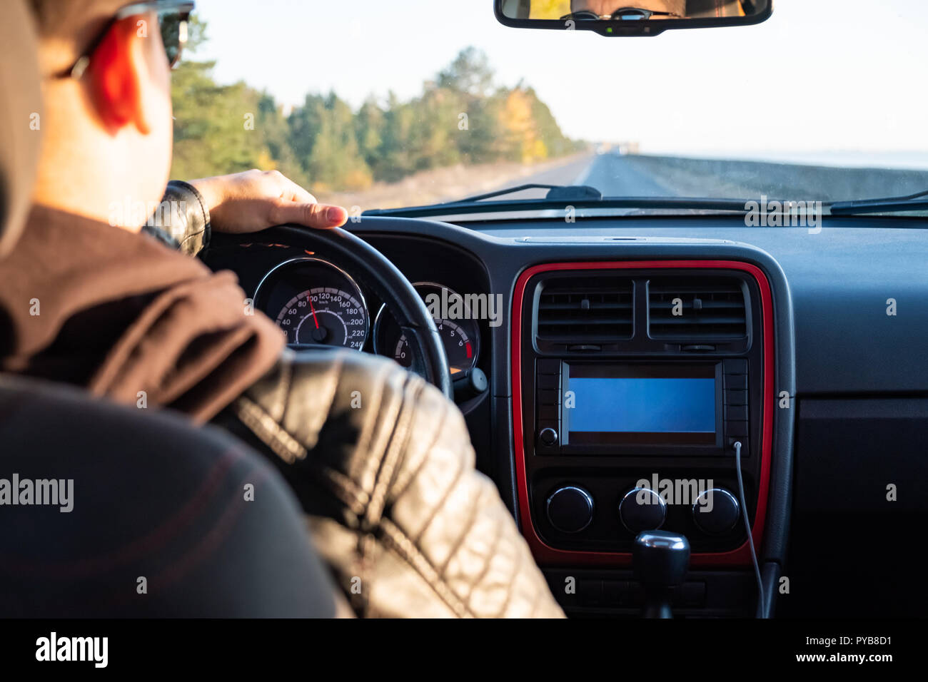 Uomo alla guida di una vettura in zona rurale, backseat vista. Driver maschio in un moderno veicolo su strada in un pomeriggio soleggiato Foto Stock