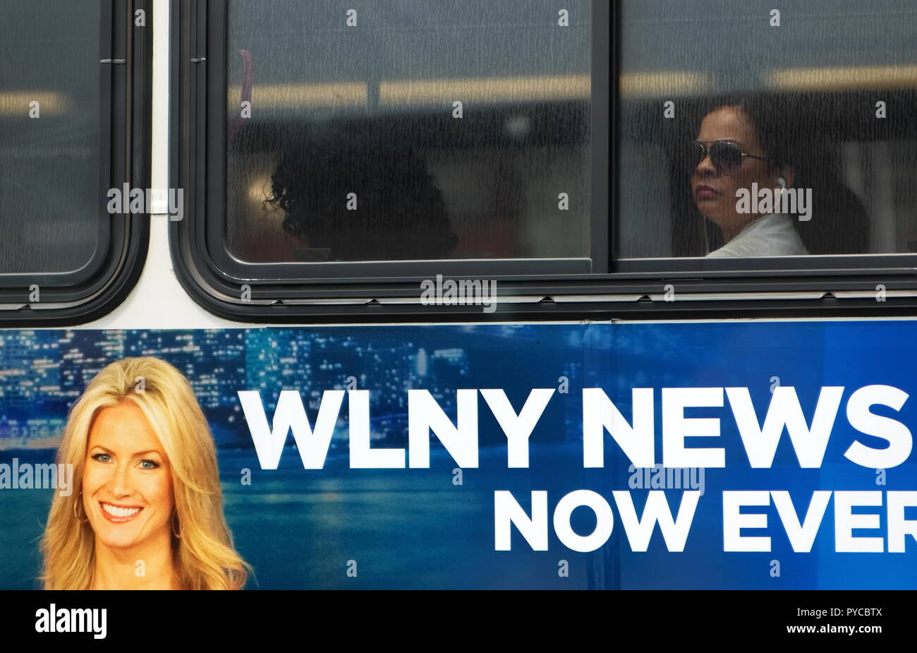 New York City, NY USA. Luglio 2014. Una signora ispanica su un autobus di città con ascolto in cuffia di mobile media e notizie locali come pubblicizzato sul bus. Foto Stock