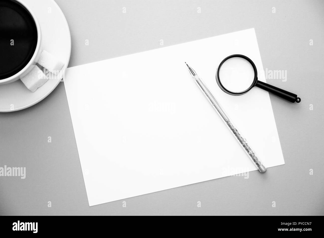 Penna carta bianca alla lente di ingrandimento e la tazza di caffè su sfondo giallo con copia vista dall'alto dello spazio immagine in bianco e nero. Foto Stock