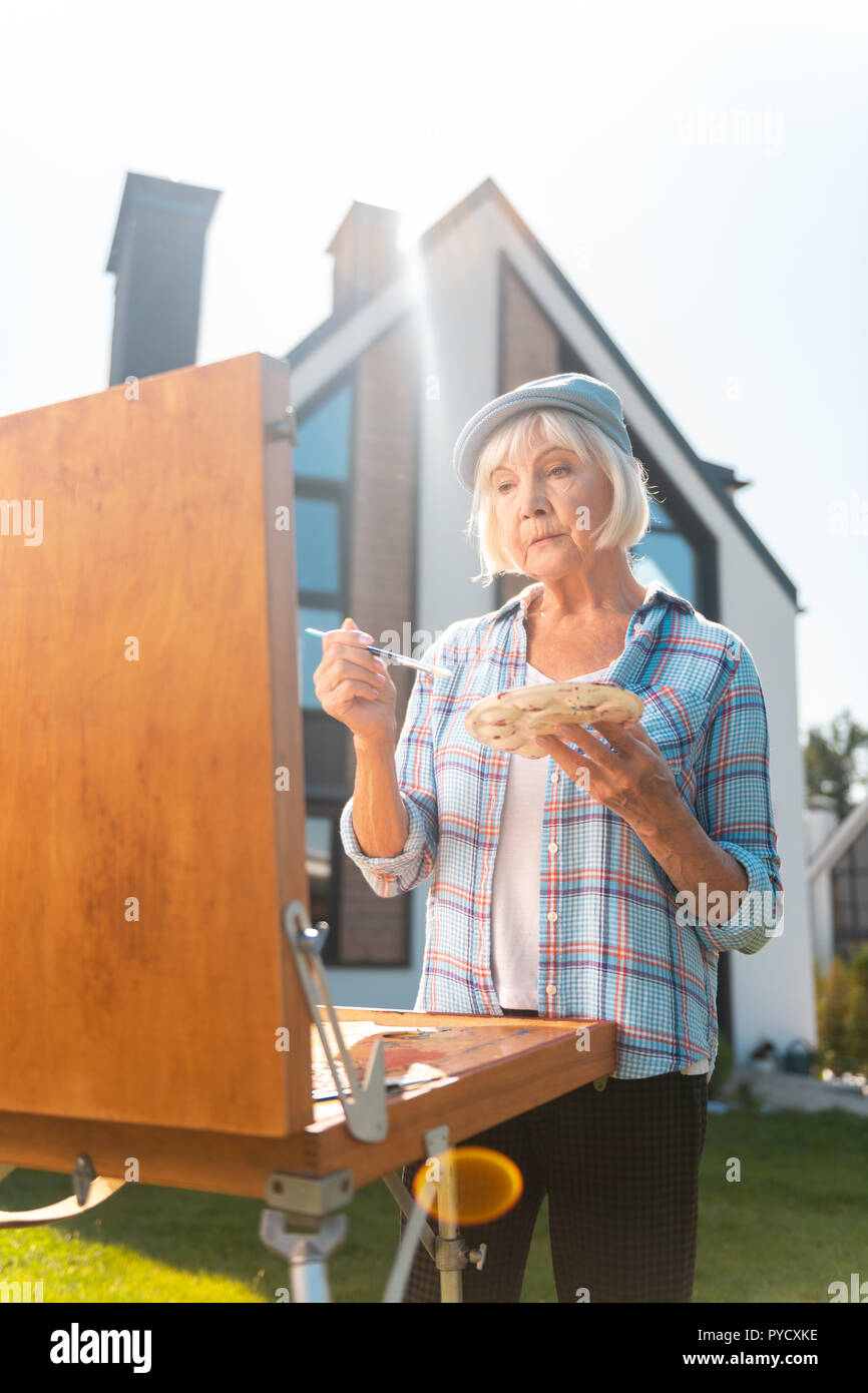 Signora indossando quadrato blu shirt holding spazzola di pittura durante il disegno esterno Foto Stock