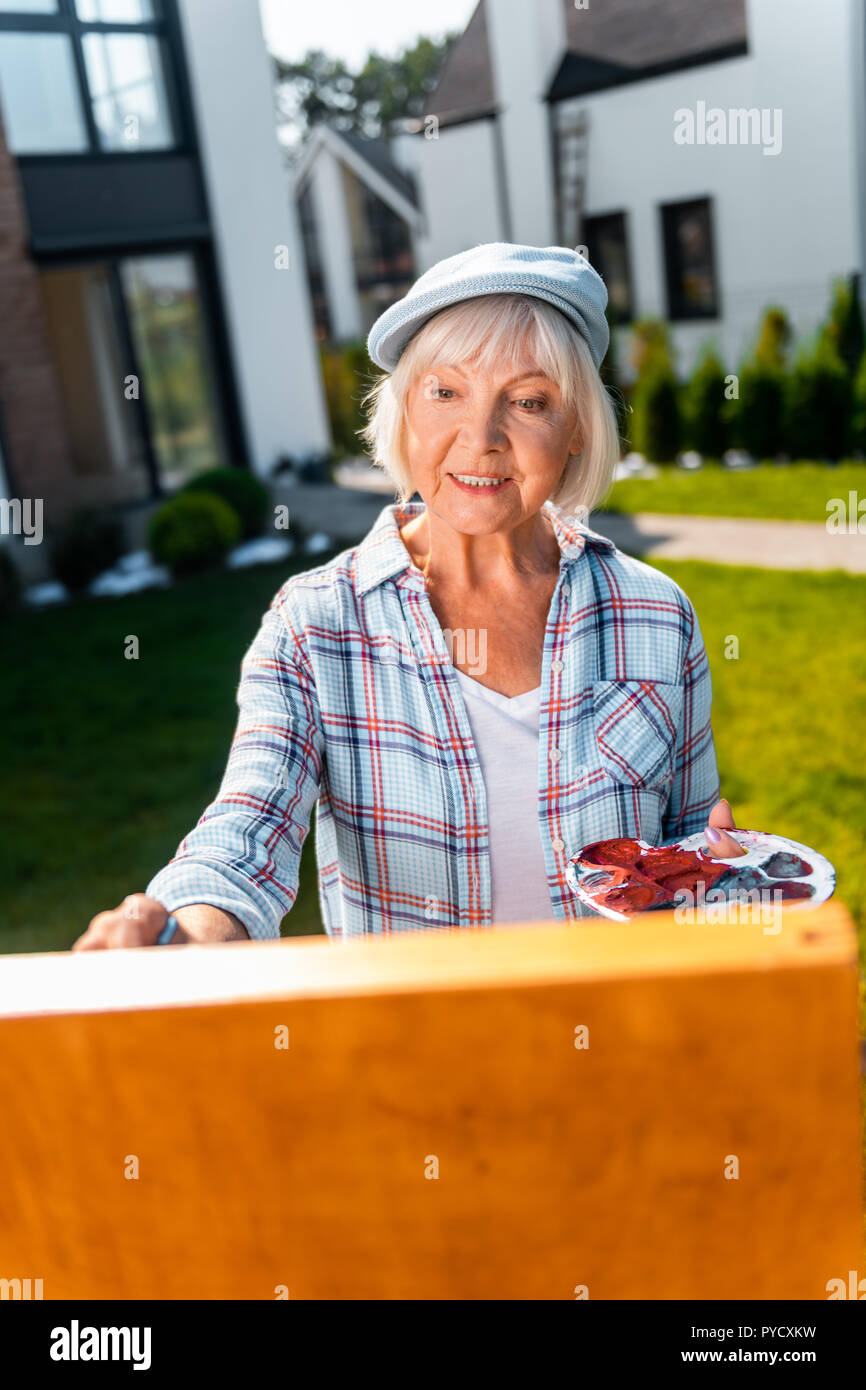 Bella signora anziana sensazione allegro durante il disegno di vita ancora nel suo giardino Foto Stock