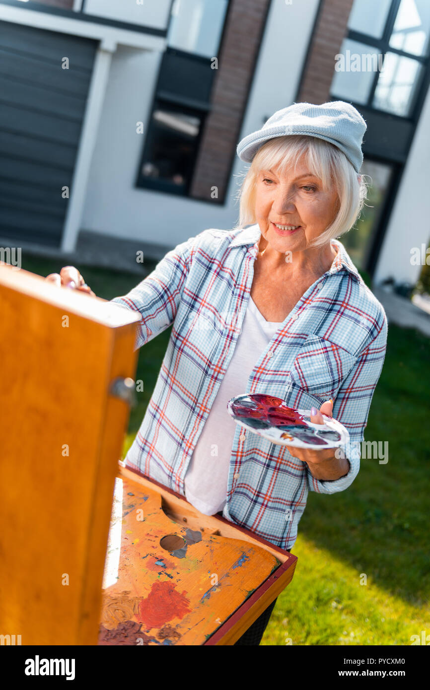Trasmissione via IR di pensionati lady holding tavolozza di colori mentre avente ispirazione e disegno Foto Stock