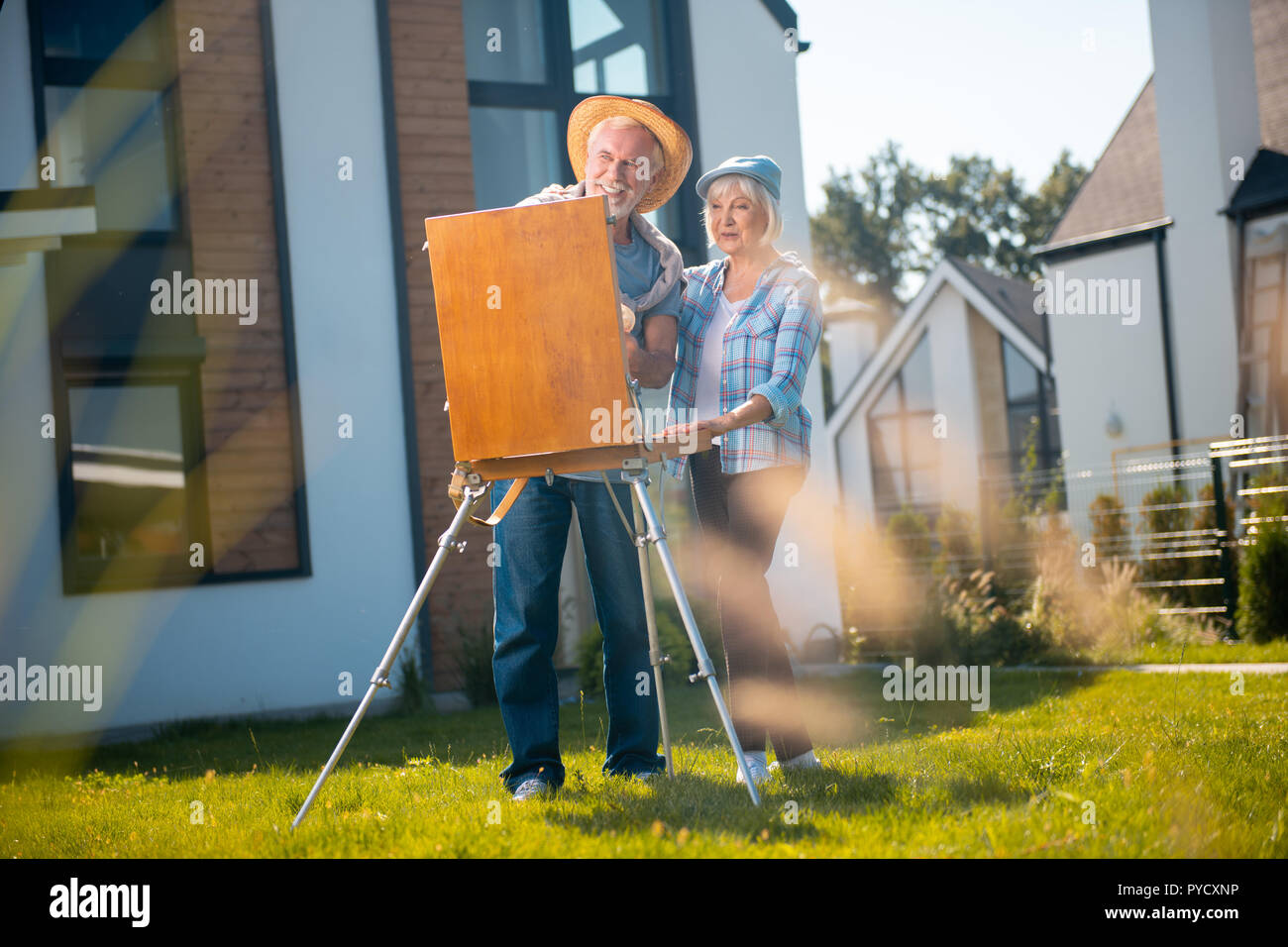 Barbuto uomo sorridente indossando cappello di paglia aiutando il suo talento di moglie natura di disegno Foto Stock
