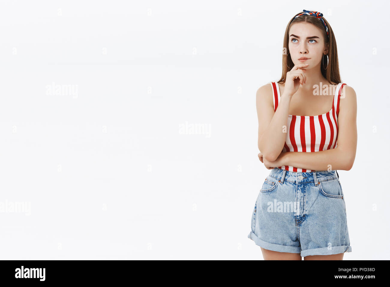 Creative ragazza cercando think up piano di lettura dei messaggi di ragazzo in piedi nel quartiere alla moda di pinup vestito con archetto e a strisce rosse top rendendo hmm look con mano sul mento, guardando verso l'alto e di pensiero Foto Stock