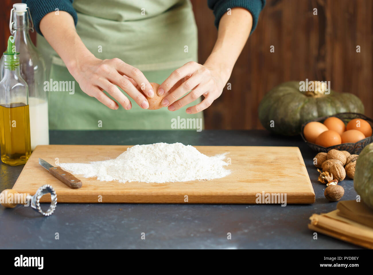 Le mani delle donne impastare. La pasticceria è il pilotaggio di un uovo in farina. Sul tavolo di legno sono gli ingredienti di cottura. Farina di zucca latte olio C Foto Stock