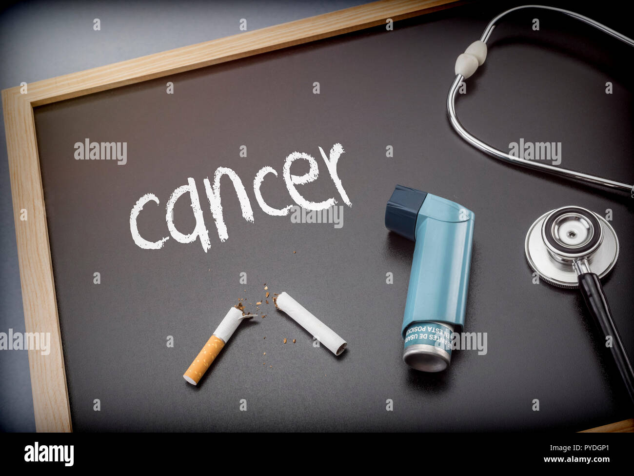 Il cancro di parola scritta in gesso su una lavagna nera accanto a uno stetoscopio e sigaretta, salbutamolo inalatore Foto Stock