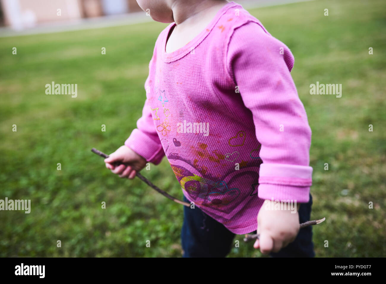 Bambina che esplora un campo di erba indossando una camicia rosa Foto Stock