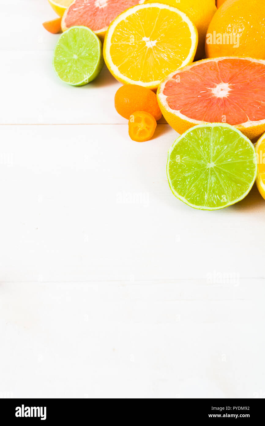 Varie intere e metà agrumi (arancio, limone, calce, pompelmo, kumquat) sul bianco sullo sfondo di legno con spazio di copia Foto Stock