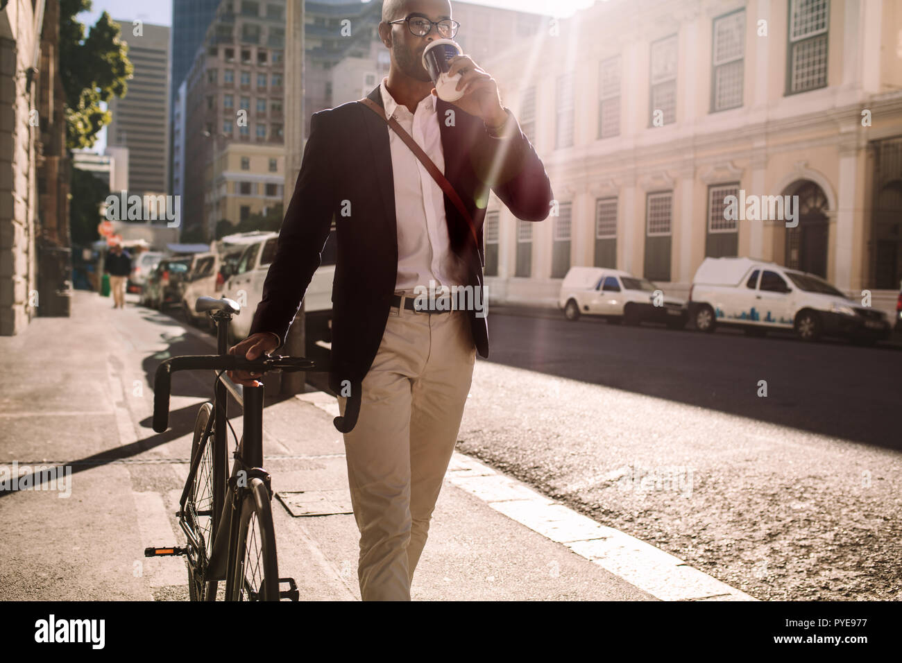 Imprenditore di andare al lavoro in bicicletta. L'uomo africano a piedi con ciclo e di bere il caffè sulla strada della citta'. Foto Stock