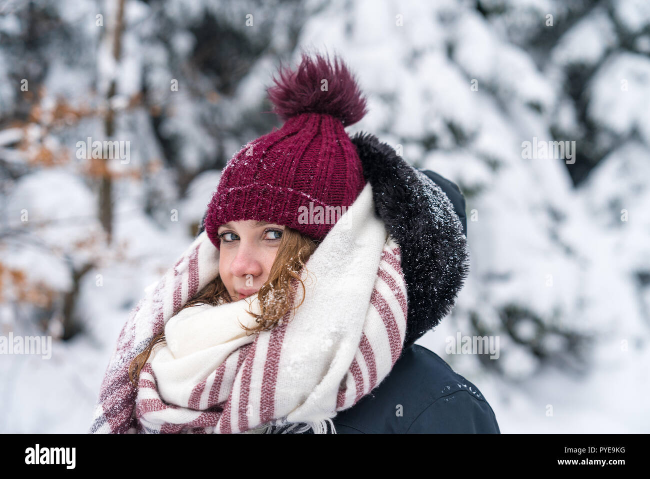 Ritratto di una giovane donna in un paesaggio invernale con vestiti caldi un cappuccio rosso e sciarpa. Foto Stock