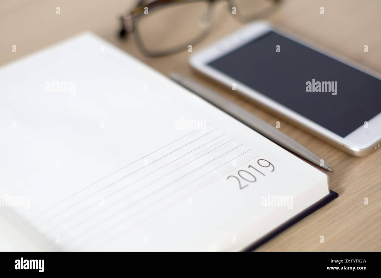 Anno Nuovo 2019 office organizer Calendario, smartphone, bicchieri e sliver penna a sfera sulla scrivania in legno. Immagine con copia spazio. Messa a fuoco selettiva. Foto Stock