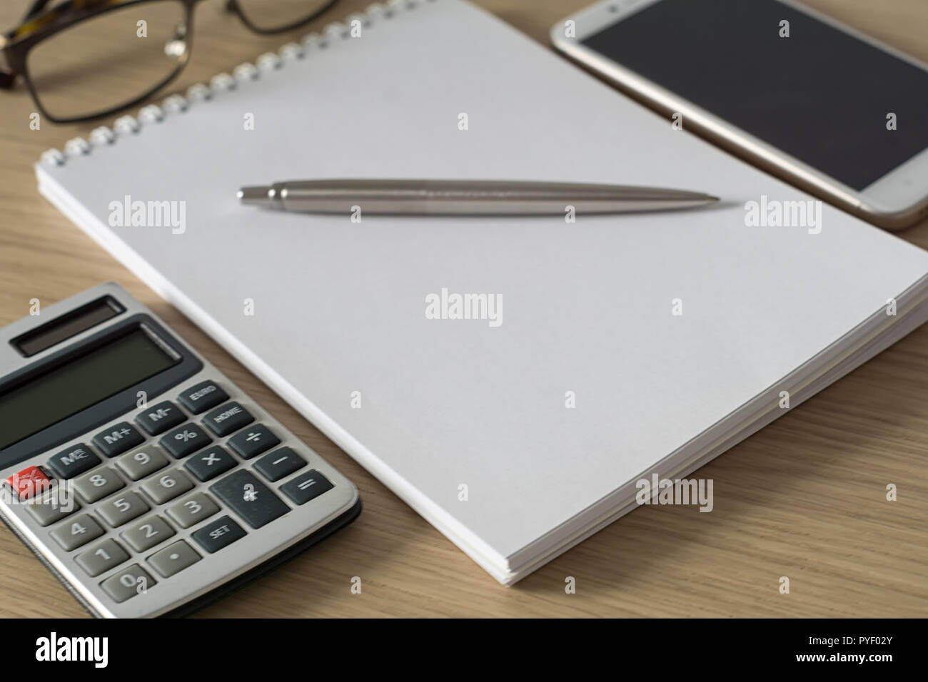 Blocco note, calcolatrice, smartphone, bicchieri e nastro in penna a sfera di legno sulla scrivania in ufficio. Immagine con copia spazio. Messa a fuoco selettiva. Foto Stock