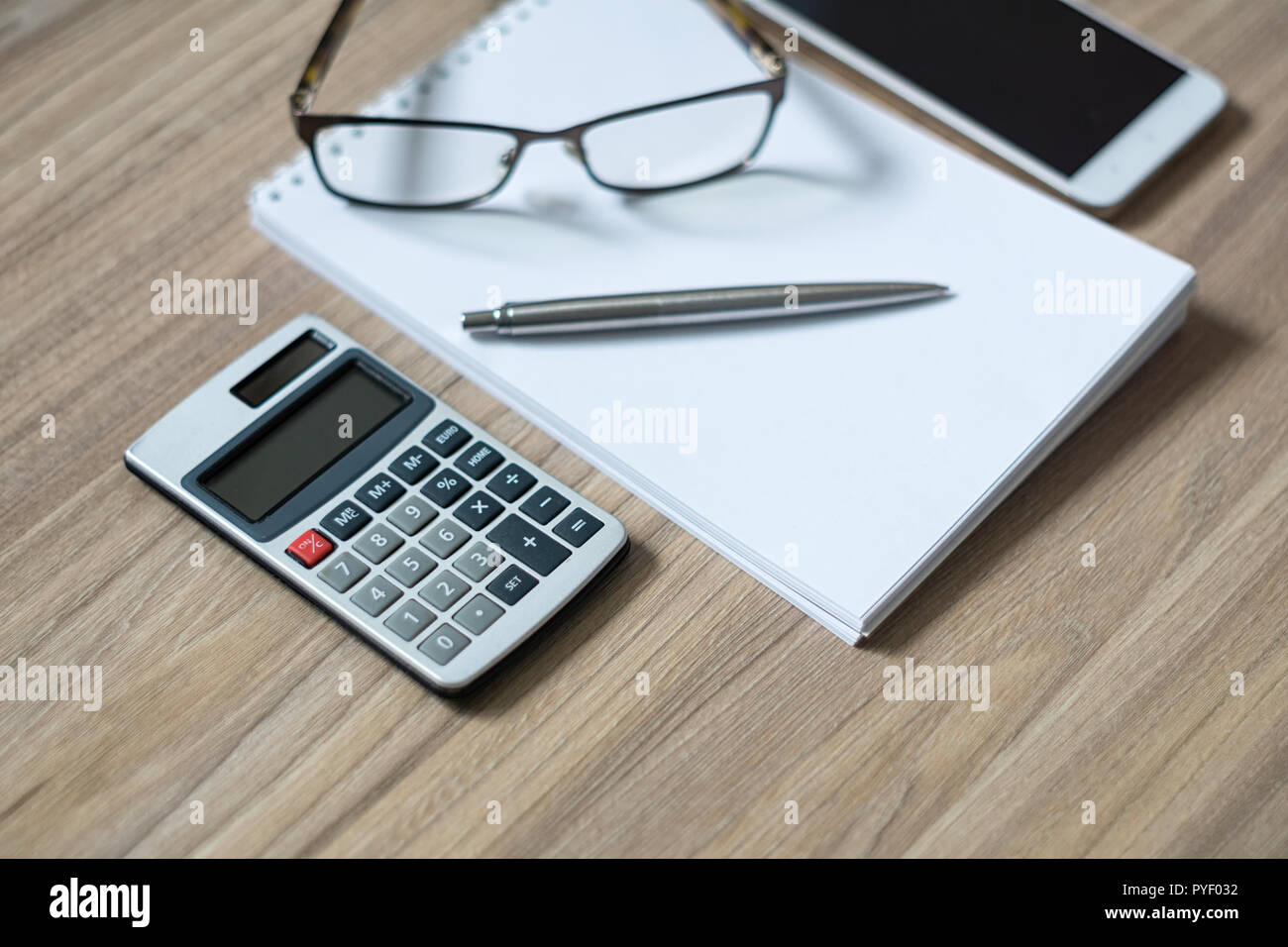 Blocco note, calcolatrice, smartphone, bicchieri e nastro in penna a sfera di legno sulla scrivania in ufficio. Messa a fuoco selettiva. Foto Stock