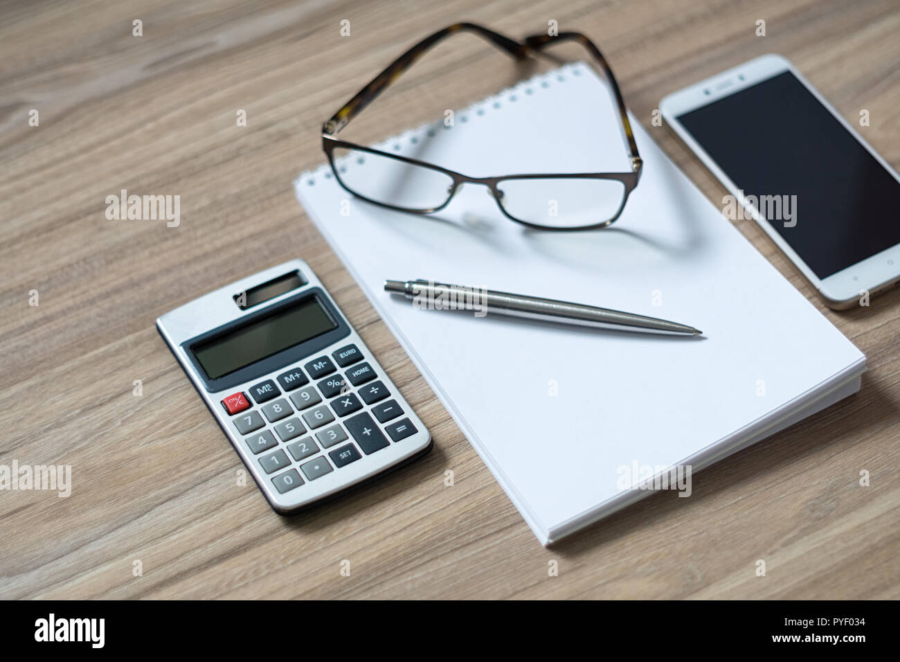 Blocco note, calcolatrice, smartphone, bicchieri e nastro in penna a sfera di legno sulla scrivania in ufficio. Messa a fuoco selettiva. Foto Stock