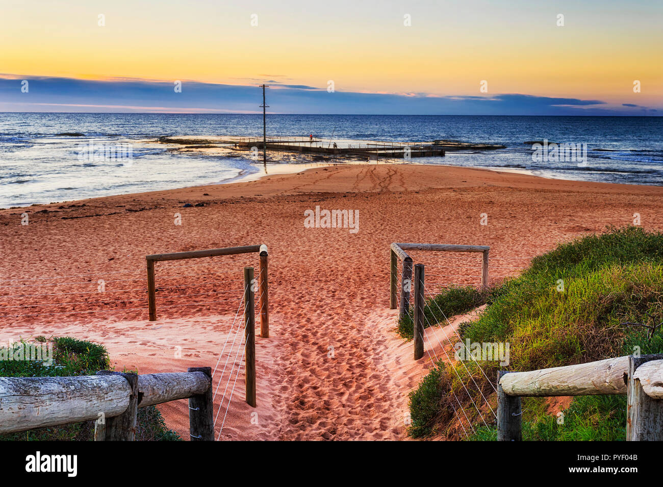 Scale di legno e fense con fili all'entrata di Mona Vale verso la spiaggia di roccia locale piscina e striscia di sabbia a sunrise con Rising Sun su oriz Foto Stock