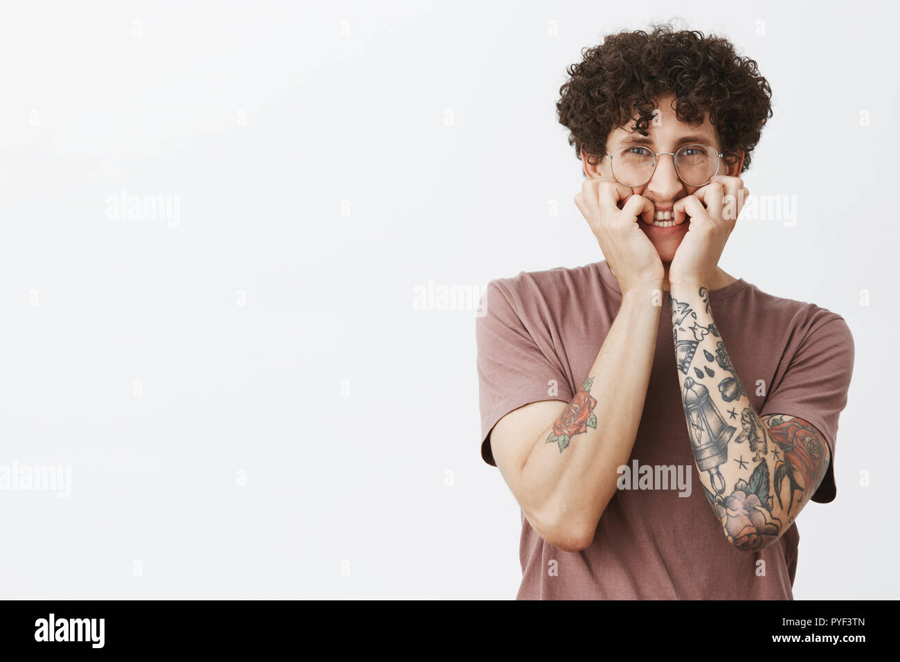 Studio shot di intensa paura e timido bella divertente comunità ragazzo con i baffi capelli ricci e tatuaggi mordere fingrnails e accigliata spaventati del film spaventoso sulla tv Foto Stock