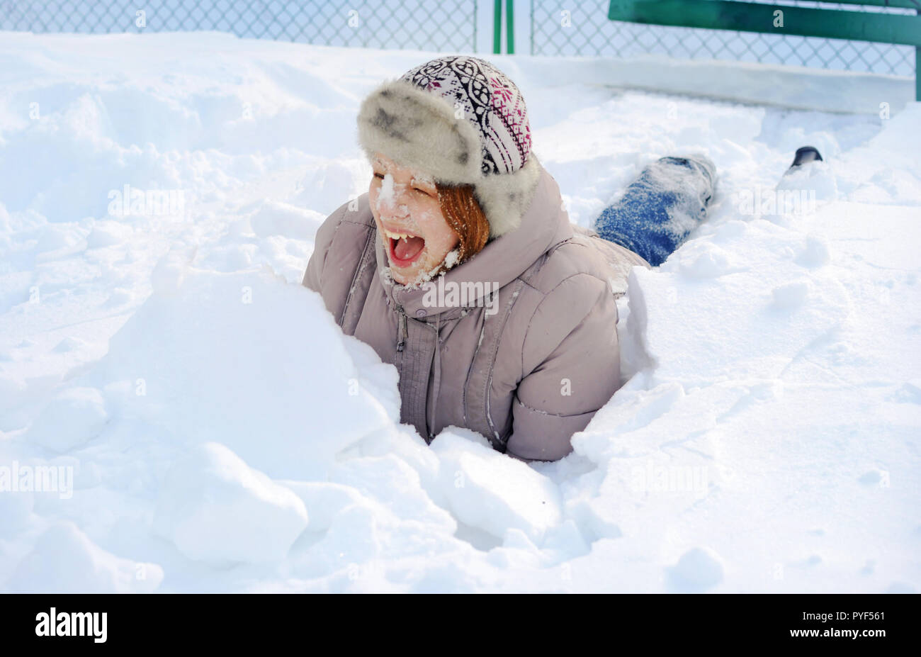 Una giovane ragazza ucraina in un parco in inverno con una sincera ampio sorriso. Ella è sdraiato nella neve heap, con il suo volto coperto di neve e la bocca aperta in Foto Stock