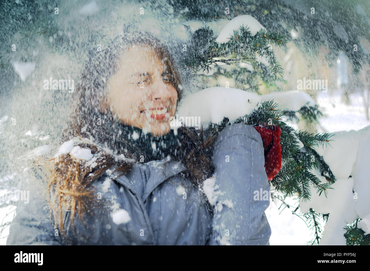 Giovane ragazza ucraina in piedi sotto i rami di abete coperto di neve nel parco. Le ragazze sono indossando inverno si chiude e squints nella gioia quando la neve Foto Stock