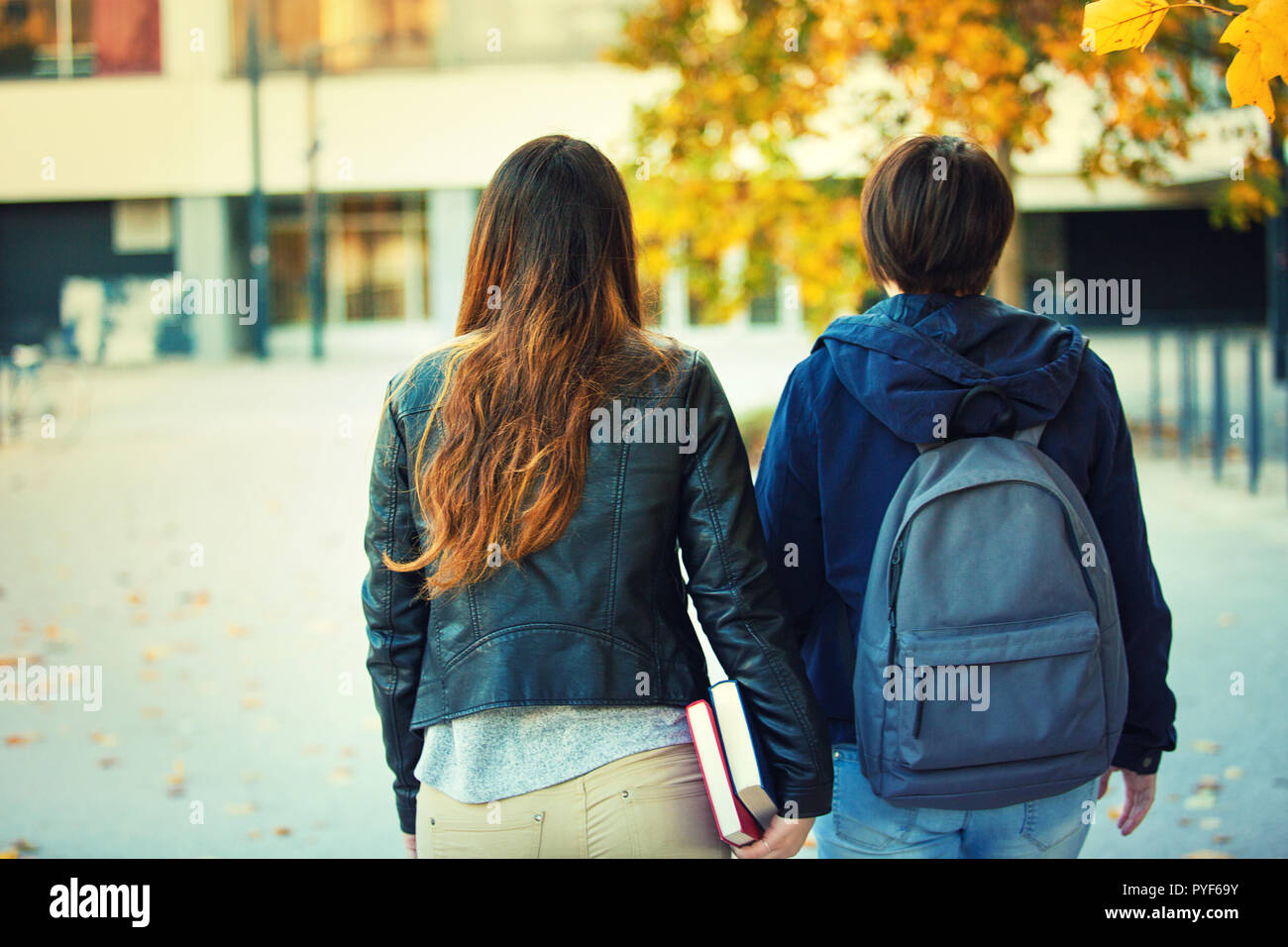 Vista posteriore di due donne gli studenti che vanno a scuola o college che porta uno zaino e con libri in mano. Autunno all'aperto amici educativo a piedi co Foto Stock