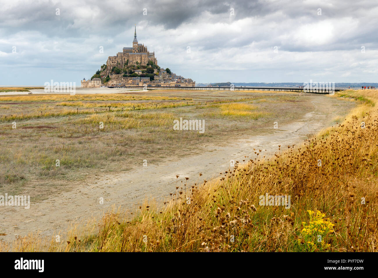 Il Mont Saint Michel villaggio fortificato e la chiesa con la bassa marea in fine di estate sotto un cielo drammatico, Normandie, Francia Foto Stock