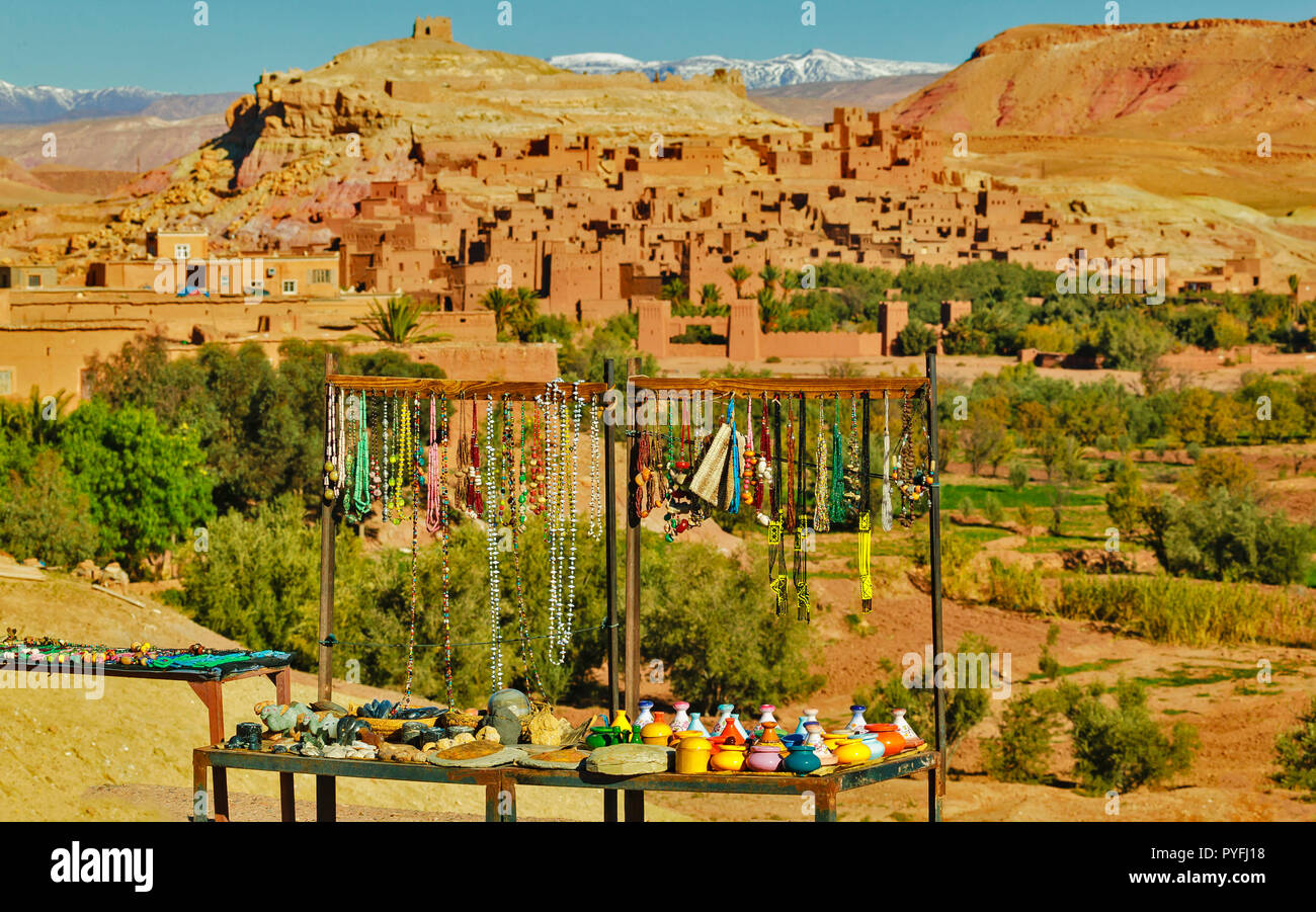 Il Marocco bancarella vendendo collane e ceramiche nella parte anteriore della parete di fango KSAR AIT BENHADDOU con neve sulle montagne Atlas Foto Stock