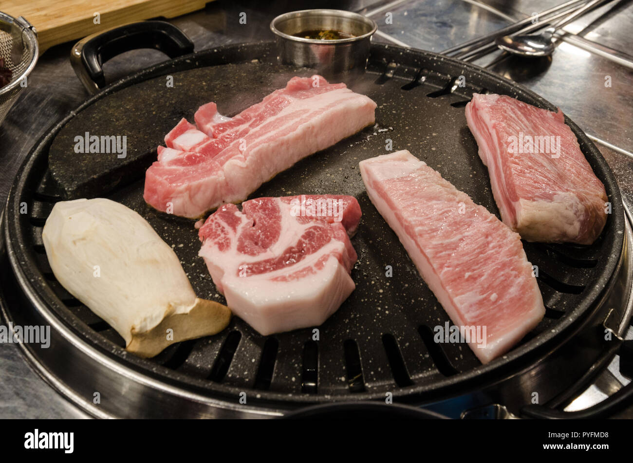 La carne di maiale per la cottura su un barbeque Coreano, un tradizionale pasto in un ristorante coreano. Foto Stock