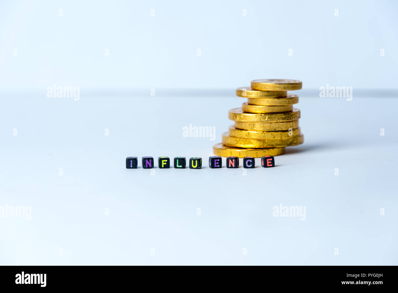 Pila di monete e testo influenza, realizzata con piccoli blocchi su sfondo bianco Foto Stock