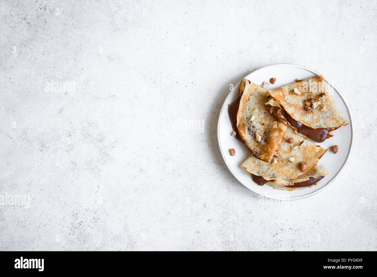 Crepes con diffusione di cioccolato e nocciole. In casa crespelle sottili per la prima colazione o per dessert su bianco, copia dello spazio. Foto Stock
