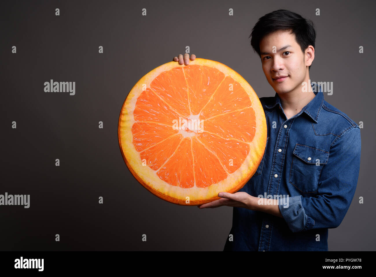 Bel giovane uomo asiatico holding arancione cuscino di frutta Foto Stock