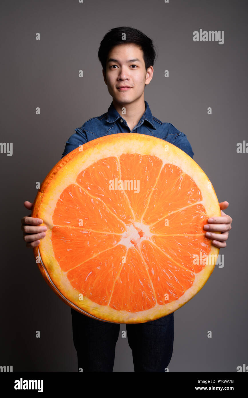 Bel giovane uomo asiatico holding arancione cuscino di frutta Foto Stock