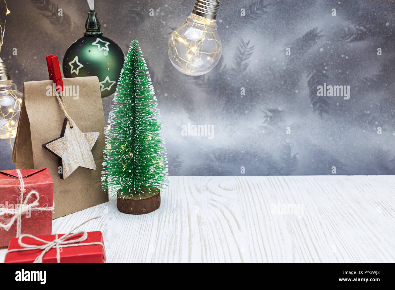 Decorazione di natale con un piccolo albero verde, carta borsa regalo, rosso confezioni regalo, sfere decorative e ghirlanda di luci Foto Stock