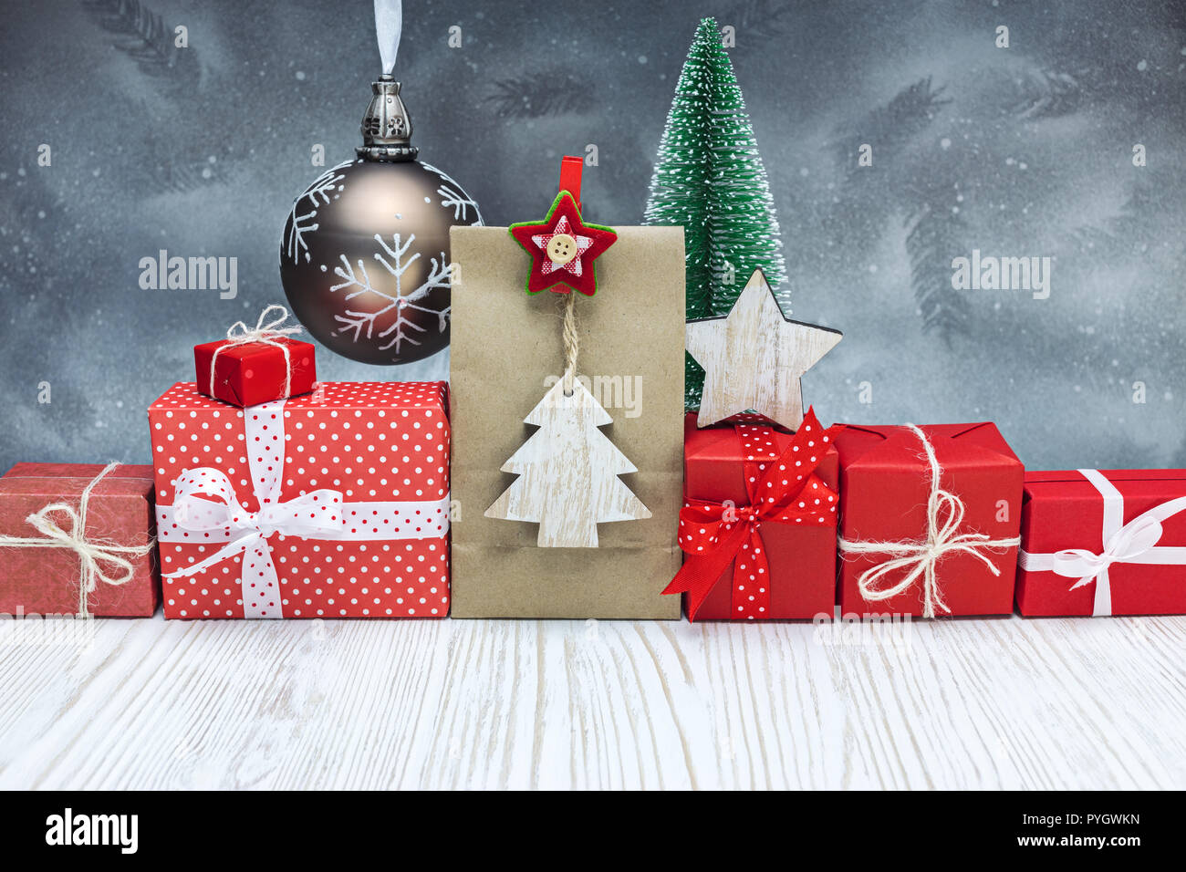 Fatte a mano scatole regalo avvolto in carta rossa, decorativi sfera di vetro con un piccolo albero di Natale sulla festosa sfondo color argento Foto Stock