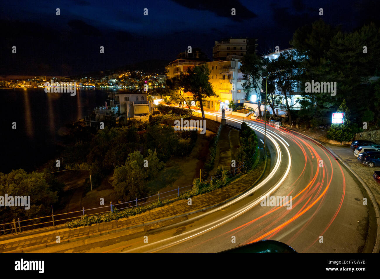 Esposizione lunga notte foto paesaggistica, cityscape presso la splendida città di mare di Saranda, Albania con effetto stella delle luci della città e acqua di mare riflessioni Foto Stock