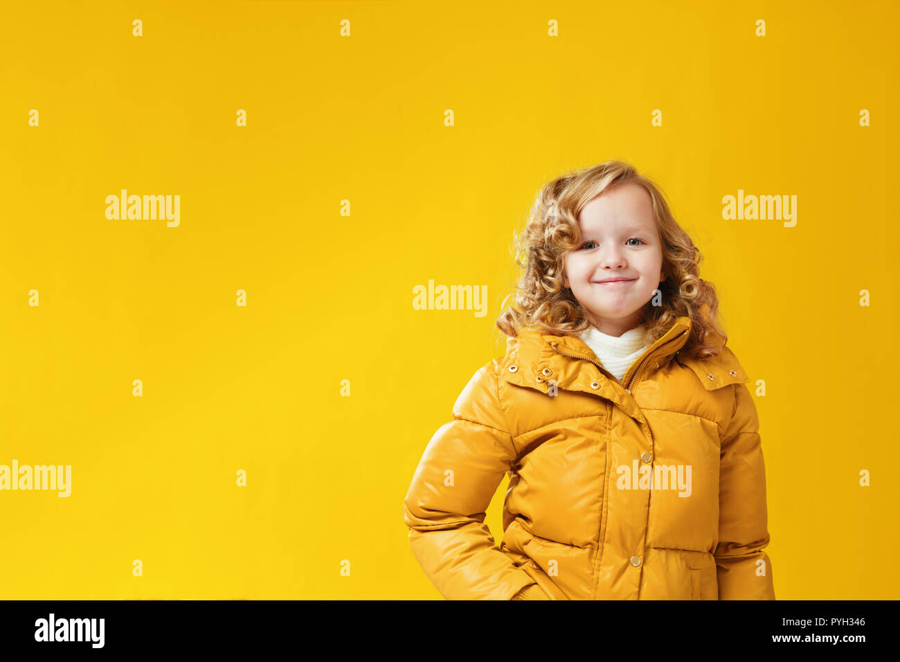 Ritratto felice bambina preschooler in una giacca invernale. Giallo su sfondo giallo. Foto Stock