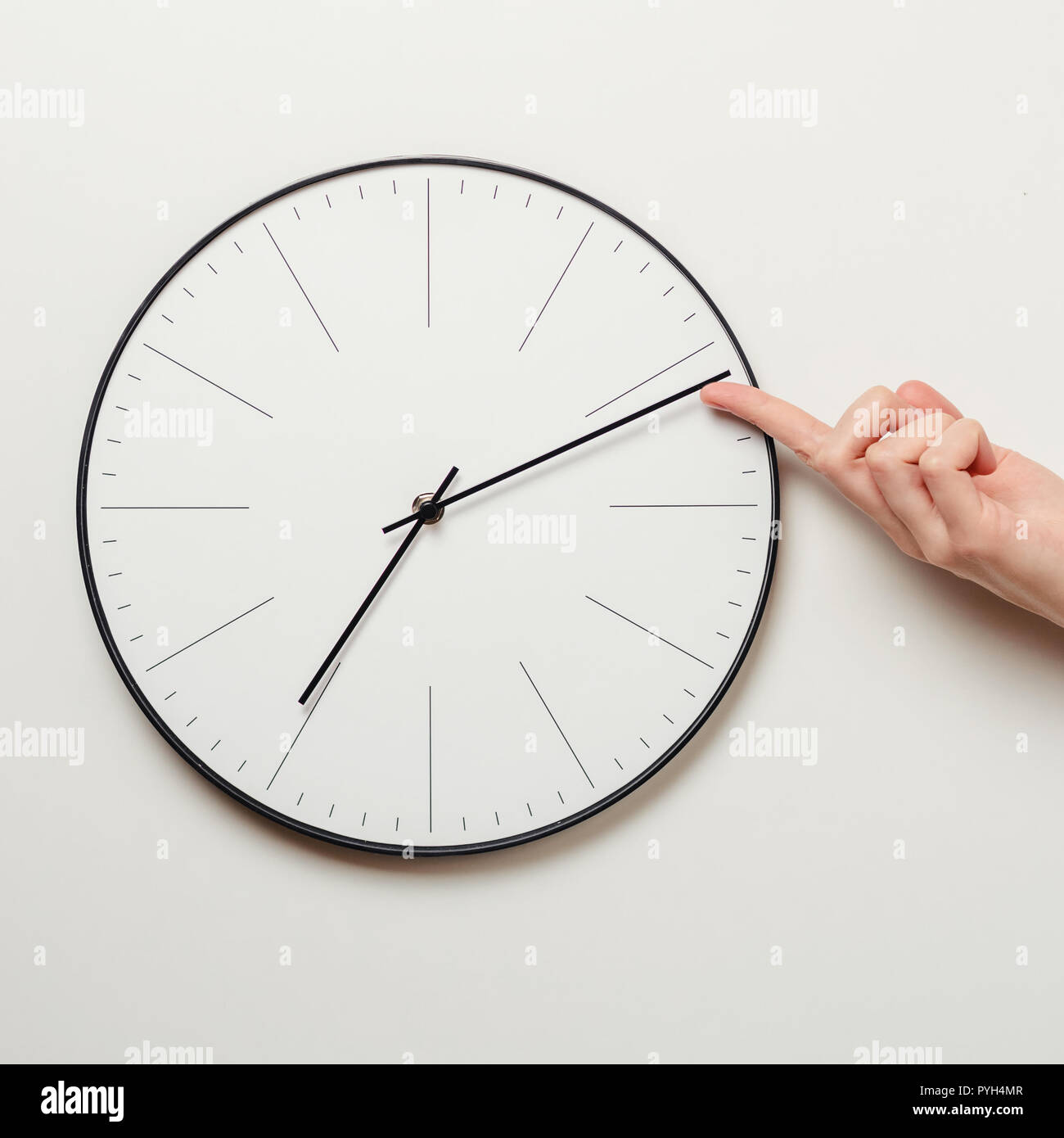 Donna mano fermare il tempo su Orologio rotondo, femmina dito prende minuto freccia dell'orologio indietro, la gestione del tempo e il concetto di scadenza Foto Stock