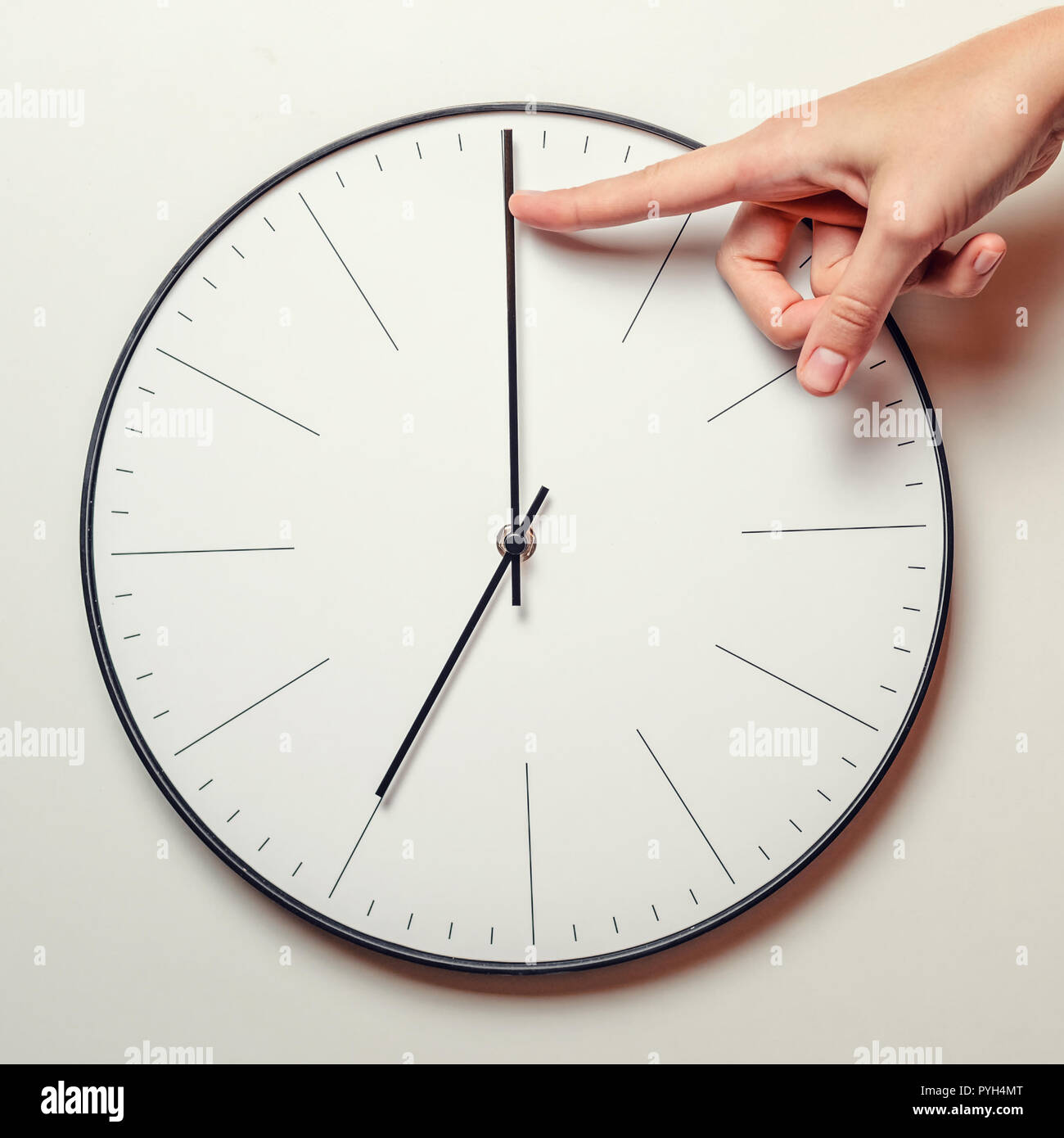 Donna mano fermare il tempo su Orologio rotondo, femmina dito prende il minuto freccia dell'orologio indietro, la gestione del tempo e il concetto di scadenza Foto Stock