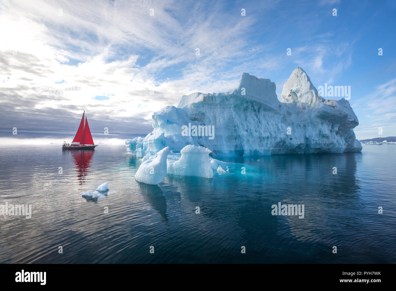 Bella rossa di barca a vela in artico accanto a un enorme iceberg che mostra la scala. Ilulissat Tourist Nature, Disko Bay, la Groenlandia. Foto Stock