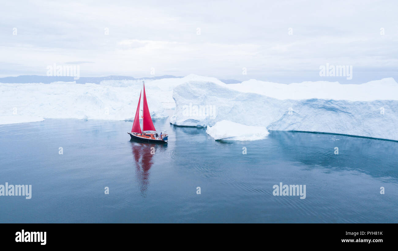 Bella rossa di barca a vela in artico accanto a un enorme iceberg che mostra la scala - Vista aerea come visto da un drone. Ilulissat Tourist Nature, Disko Bay, Greenlan Foto Stock