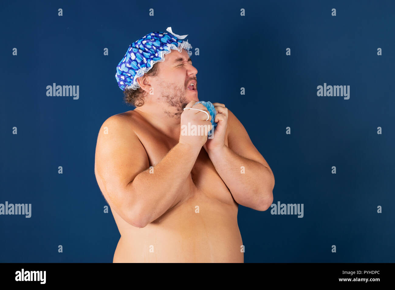 Funny uomo grasso nel tappo blu e con spugna sotto la doccia Foto Stock