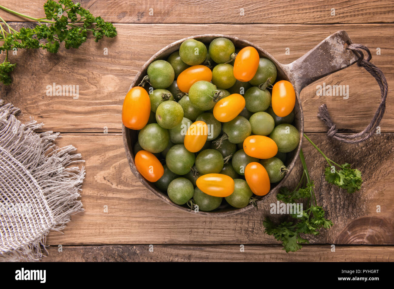 Lay piatto con verde e giallo arancione varietà di pomodoro nel recipiente rotondo sul legno strutturata la superficie del tavolo verde con foglie di prezzemolo. Messa a fuoco selettiva. Foto Stock