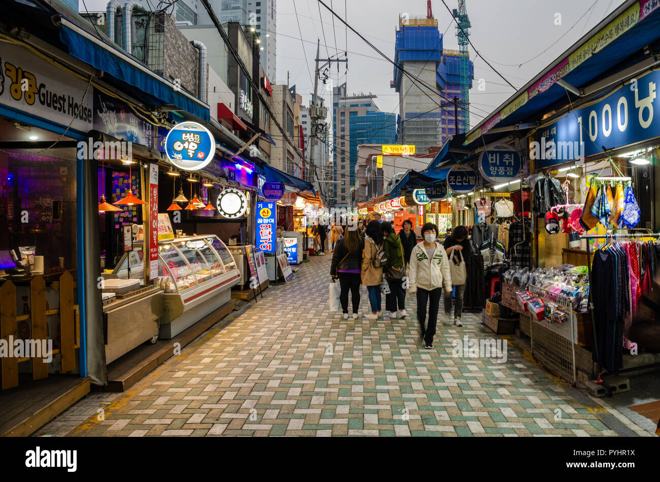 Le persone camminare attraverso Haeundae Maerket al tramonto come si diventa scuro e le luci si accendono. Haeundae, Busan, Corea del Sud. Foto Stock