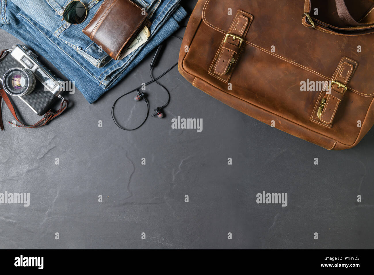 Accessori per piano di viaggio, viaggio vacanze, turismo - business borsa in pelle e jeans blu con fotocamera vintage sulla pietra nera sfondo. vista superiore e Foto Stock